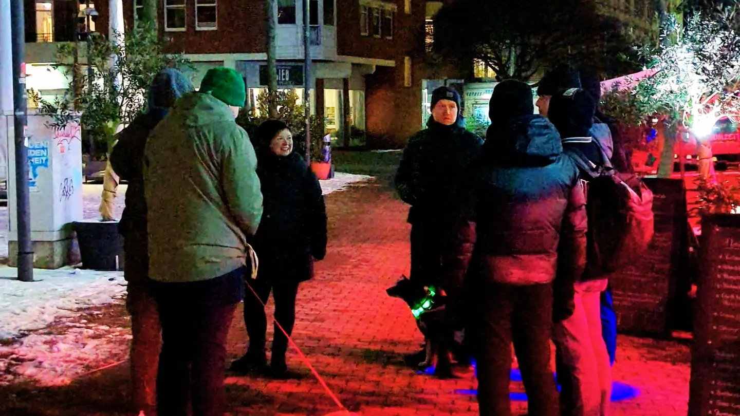 Abendlicher Beleuchtungsrundgang der Grünen auf dem Hansaplatz in St. Georg – Gruppe diskutiert unter buntem Licht der umliegenden Gastronomie
