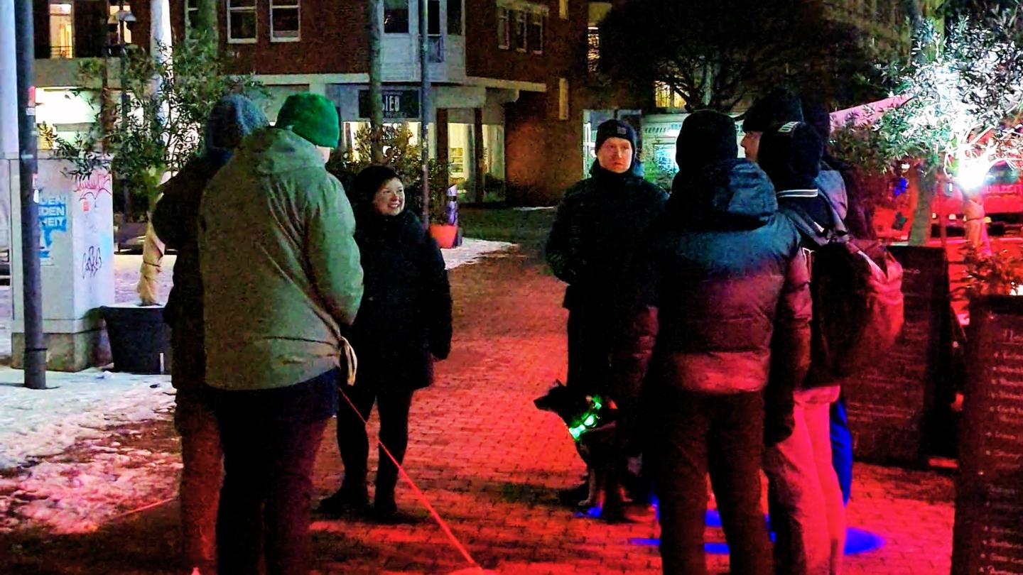 Abendlicher Beleuchtungsrundgang der Grünen auf dem Hansaplatz in St. Georg – Gruppe diskutiert unter buntem Licht der umliegenden Gastronomie