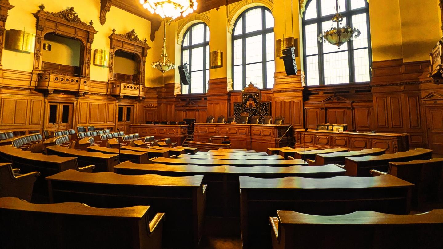 Leerer Plenarsaal im Hamburger Rathaus mit historischer Holzvertäfelung und gebogenen Abgeordnetensitzen